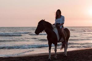 femme en vêtements d'été aime monter à cheval sur une belle plage de sable au coucher du soleil. mise au point sélective photo