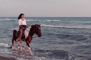 femme en vêtements d'été aime monter à cheval sur une belle plage de sable au coucher du soleil. mise au point sélective photo
