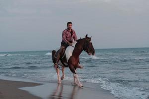 un homme moderne en vêtements d'été aime monter à cheval sur une belle plage de sable au coucher du soleil. mise au point sélective photo