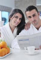 couple heureux lisant le journal dans la cuisine au petit déjeuner photo