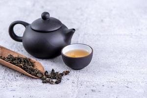thé chaud dans une théière noire et des tasses et des feuilles de thé sèches sur fond de ciment gris clair, gros plan, concept de conception d'espace de copie.
