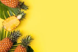 bel ananas sur des feuilles de monstera de palmiers tropicaux isolés sur fond jaune orange pastel clair, vue de dessus, à plat, au-dessus des fruits d'été. photo