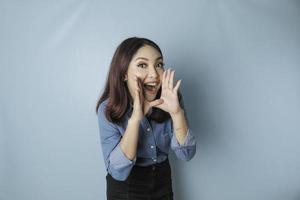 belle jeune femme portant une chemise bleue criant et criant fort sur le côté avec une main sur sa bouche. notion de communication. photo