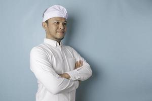 portrait d'un homme balinais souriant confiant debout avec les bras croisés et regardant la caméra isolée sur fond bleu, vêtu d'une chemise bleue photo