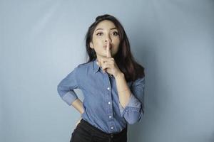 portrait d'une jeune femme asiatique dites être tranquille, chut avec un visage sérieux, chut avec le doigt pressé sur les lèvres, isolé par fond bleu photo