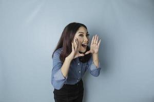 belle jeune femme portant une chemise bleue criant et criant fort sur le côté avec une main sur sa bouche. notion de communication. photo