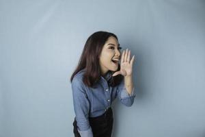 belle jeune femme portant une chemise bleue criant et criant fort sur le côté avec une main sur sa bouche. notion de communication. photo