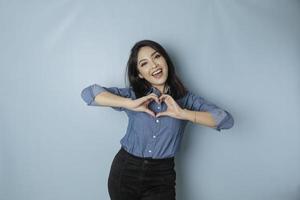 une jolie jeune femme asiatique portant une chemise bleue se sent heureuse et un geste de coeur aux formes romantiques exprime des sentiments tendres photo