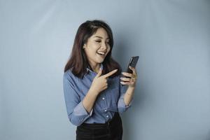 un portrait d'une femme asiatique heureuse sourit et tient son smartphone portant une chemise bleue isolée par un fond bleu photo
