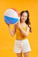 belle femme asiatique décontractée avec des accessoires de plage tenant une balle colorée sur fond orange