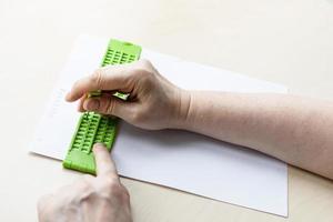 main imprime des mots en braille avec ardoise et stylet photo