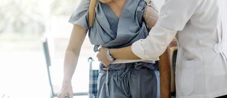 jeune physiothérapeute asiatique travaillant avec un vieil homme sur le travail à l'aide d'un déambulateur dans le couloir d'une maison de retraite photo