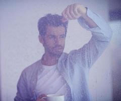 un jeune homme détendu boit le premier café du matin avec des gouttes de pluie sur la fenêtre photo