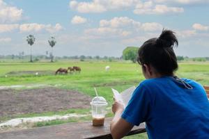 vue arrière d'une femme lisant un livre et buvant du café tout en prenant des vacances sur des terres agricoles photo