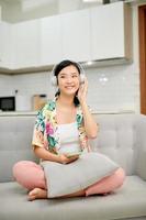 portrait belle jeune femme asiatique utiliser un téléphone mobile intelligent avec un casque pour écouter de la musique sur un canapé dans le salon photo
