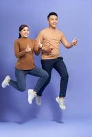 photo d'un jeune couple d'amoureux heureux sautant isolé sur fond violet montrant les pouces vers le haut.