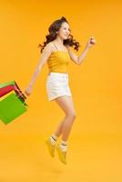 joyeuse adolescente d'été portant des sacs à provisions et sautant dans l'air sur fond orange, prise de vue en pied avec espace de copie photo