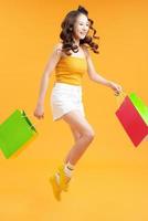 Jolie femme souriante et élégante accro du shopping sautant en cours d'exécution tenant des sacs à provisions sur fond jaune isolé photo