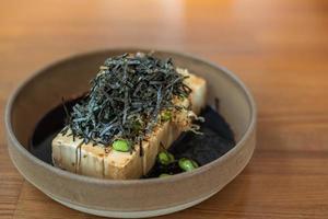 gros plan de tofu froid avec sauce soja dashi, garniture d'algues et edamame dans un bol en faïence de style japonais.
