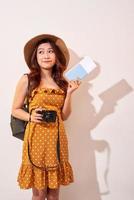 femme touristique expressive en vêtements décontractés d'été, chapeau tenant un passeport, billets isolés sur fond beige. femme voyageant à l'étranger pour voyager le week-end. concept de voyage en avion photo