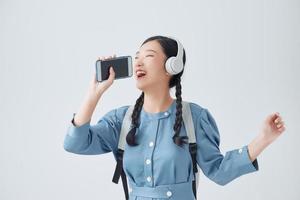 femme asiatique excitée posant isolée sur fond blanc écoutant de la musique avec des écouteurs dansant en chantant. photo