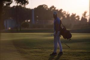 golfeur marchant et portant un sac de golf au beau coucher de soleil photo