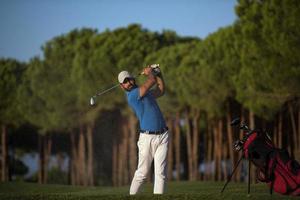 golfeur frappant un bunker de sable tourné au coucher du soleil photo