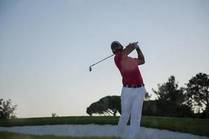 golfeur frappant un bunker de sable tourné au coucher du soleil photo