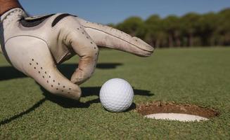 la main de l'homme met la balle de golf dans le trou photo