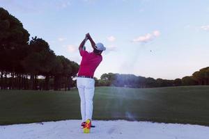 golfeur frappant un bunker de sable tourné au coucher du soleil photo