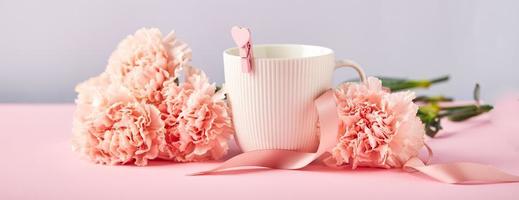 bouquet d'oeillets roses et tasse blanche. concept de conception de voeux de vacances avec bouquet d'oeillets sur fond rose et bleu photo