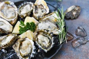 huîtres fraîches fruits de mer sur fond de plaque noire - coquille d'huître ouverte avec épices aux herbes citron romarin servi table et glace fruits de mer sains dîner d'huîtres crues au restaurant cuisine gastronomique photo