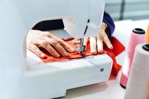 Senior woman tailleur travaillant à l'usine de couture - couturière faisant la machine à coudre coudre du tissu dans la salle d'exposition des vêtements de mode et du fil à coudre photo