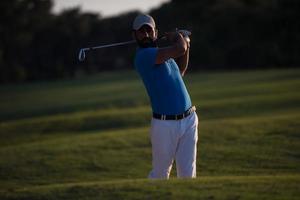 golfeur frappant un bunker de sable tourné au coucher du soleil photo