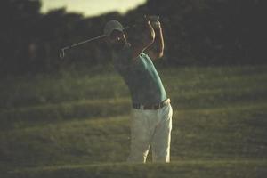 golfeur frappant un bunker de sable tourné au coucher du soleil photo