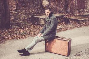 portrait d'homme de style vintage assis sur une valise en cuir à l'extérieur. photo