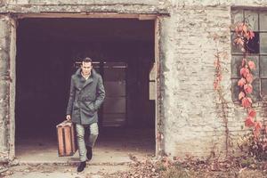 homme confiant portant une vieille valise en cuir et sortant d'un bâtiment abandonné. photo