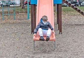 enfant ludique avec masque facial ayant sur un toboggan à l'aire de jeux. photo