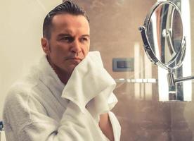homme essuyant le visage avec une serviette en coton après le rasage dans la salle de bain. photo