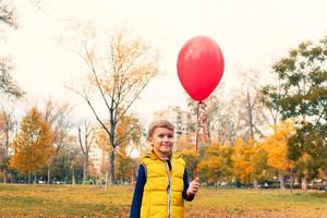 enfant mignon avec ballon rouge dans le parc d'automne. photo