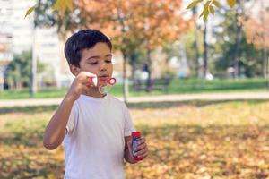 petit garçon soufflant des bulles avec une baguette à bulles dans le parc d'automne. photo