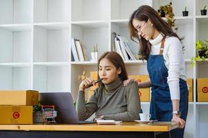 deux femmes heureuses qui vendent des produits en ligne créent une petite entreprise à l'aide d'un ordinateur portable, calculent les prix et se préparent à l'affranchissement. photo