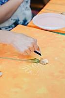 femme peignant un pissenlit sur fond orange en utilisant une manière créative de dessiner avec une carte. cours de peinture, apprentissage du dessin à la peinture acrylique, vertical. photo