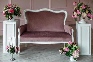 banc vintage en velours de bois à côté de tables de chevet blanches et de bouquets de fleurs photo