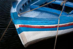 gros plan et détail d'un vieux bateau de pêche en bois peint en bleu, rouge et blanc. le bateau se tient dans l'eau sombre et est attaché au rivage avec des cordes. photo
