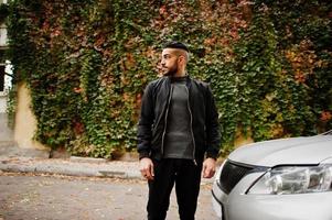 portrait d'un homme à la barbe arabe élégant portant un col roulé gris et un jaket noir. un mec modèle arabe se tient près de sa voiture. photo
