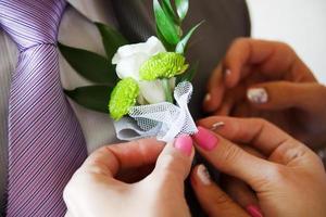 la mariée met le marié sur la boutonnière du rose et de la rose blanche le jour du mariage photo