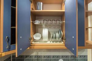 ensemble d'assiettes, tasses, couteaux, fourchettes et verres à vin sur l'étagère de l'armoire de cuisine photo