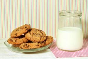 biscuits savoureux et pot de lait sur fond rayé coloré photo