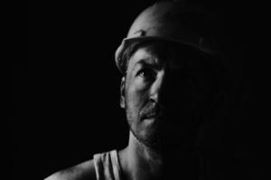 mineur de charbon sale dans un casque jaune sur fond sombre sur une photo en noir et blanc.